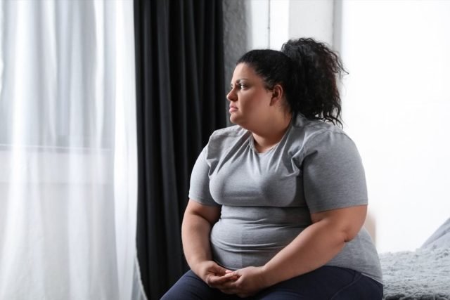 Depressed overweight woman on bed at home