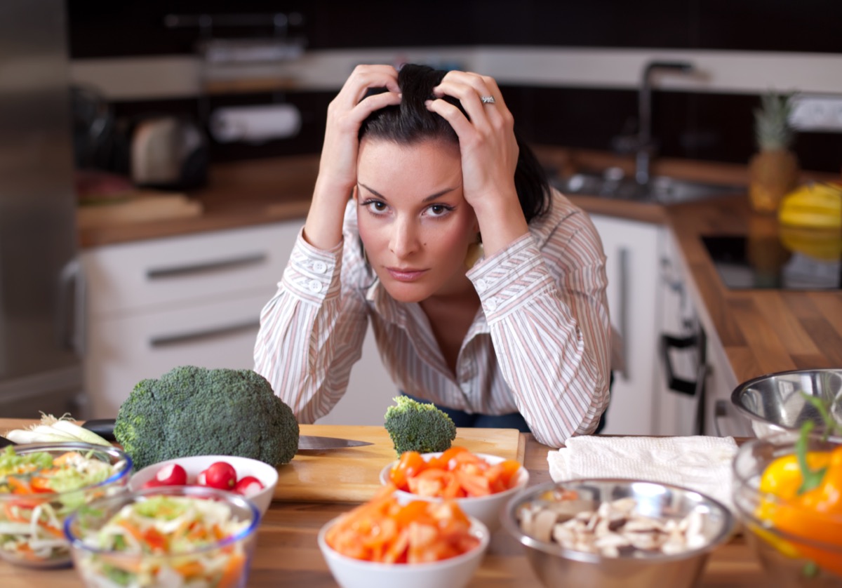 Sad woman looking out at salad bowls in her kitchen.