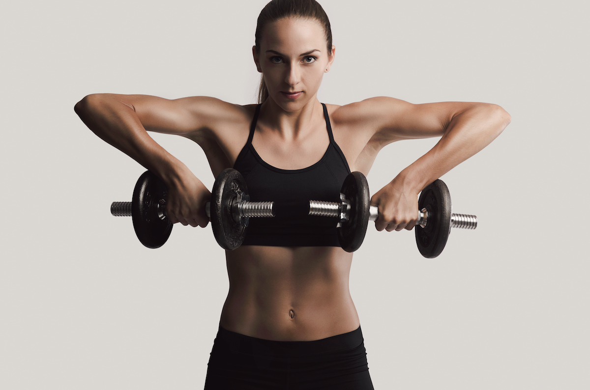 Beautiful young woman in a workout gear lifting dumbbells