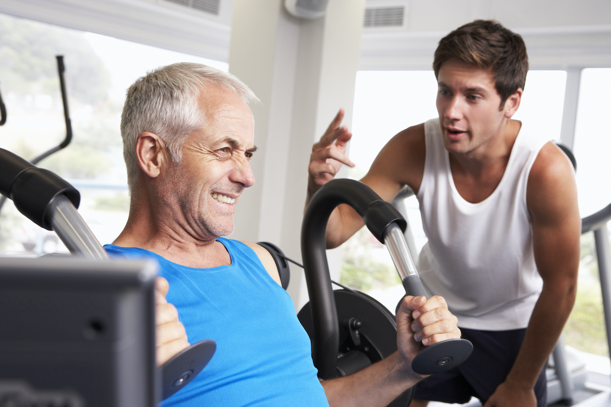 Middle Aged Man Being Encouraged By Personal Trainer In Gym