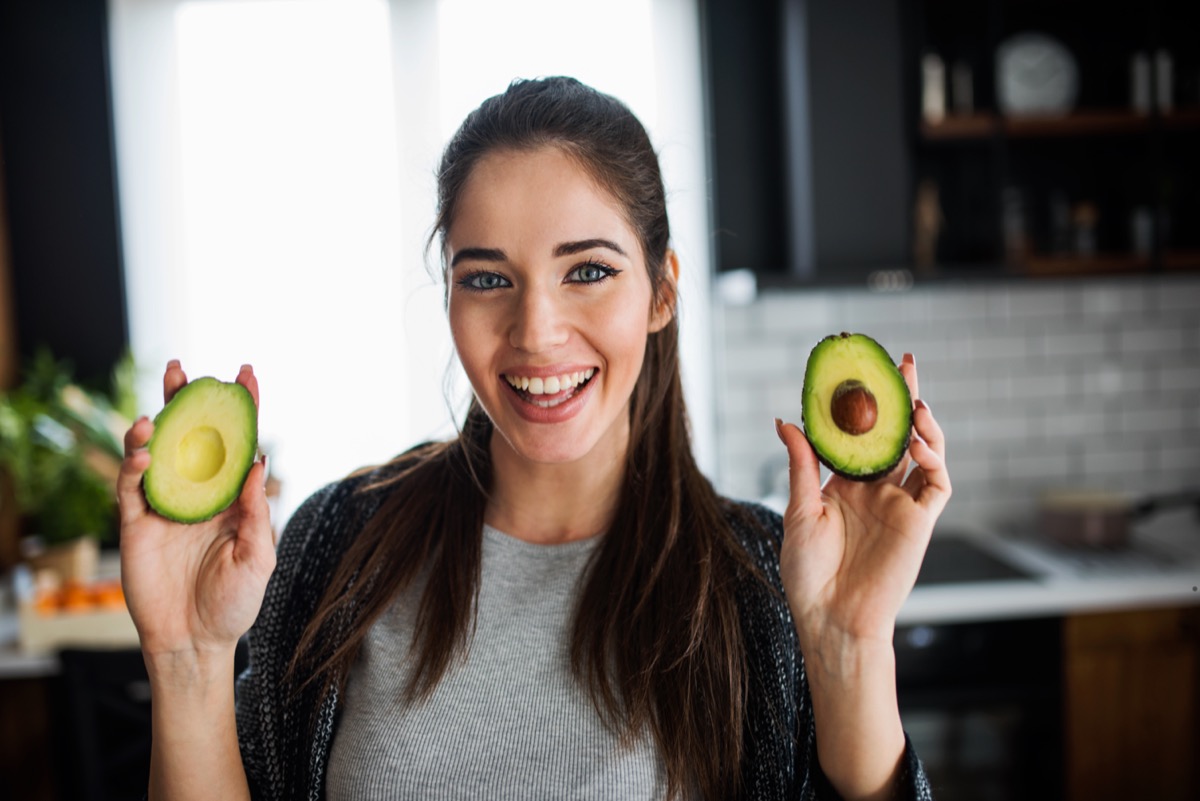 Smiling woman in her kitchen holding avocado.