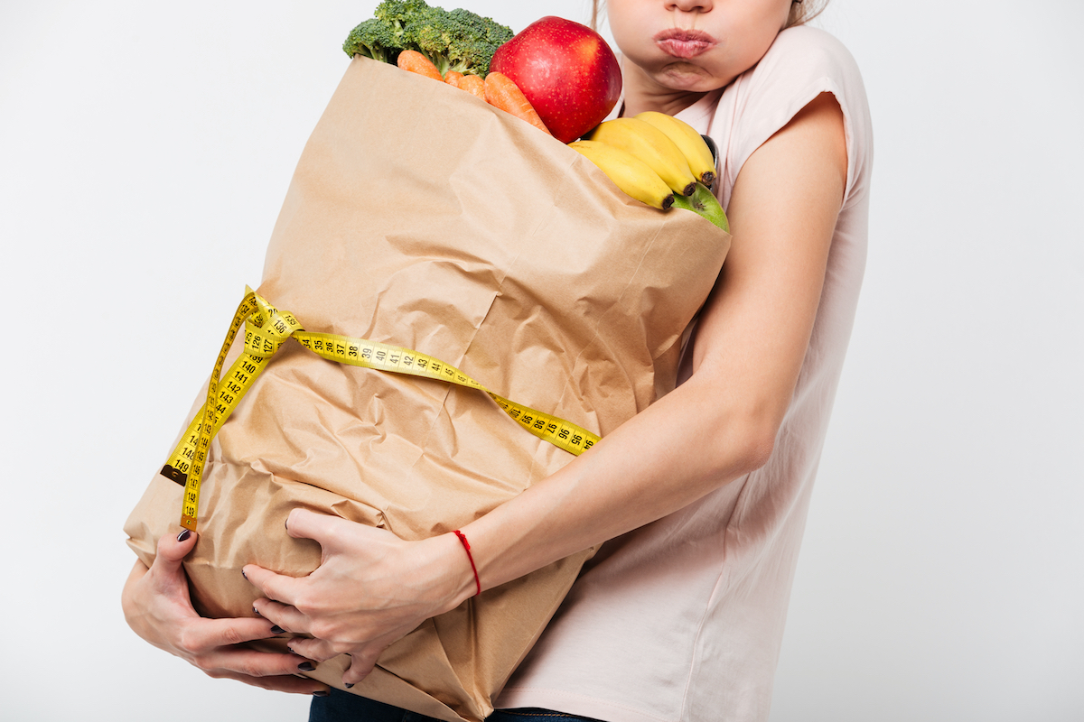 Close up of a woman holding heavy bag with groceries wrapped with a measuring tape isolated over white background