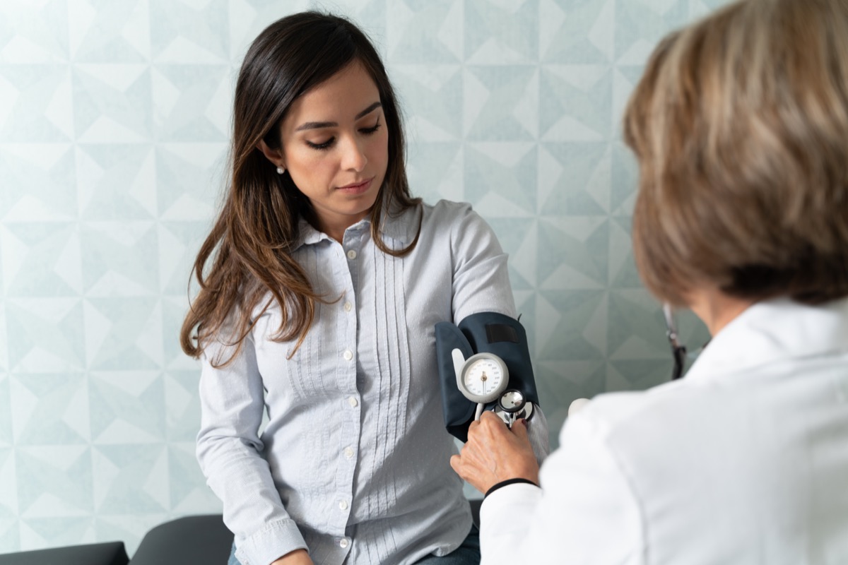 Senior female gynecologist checking woman with blood pressure gauge in hospital.