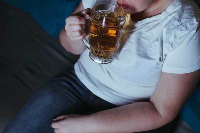 A woman wearing a white T-shirt is drinking beer in the dark