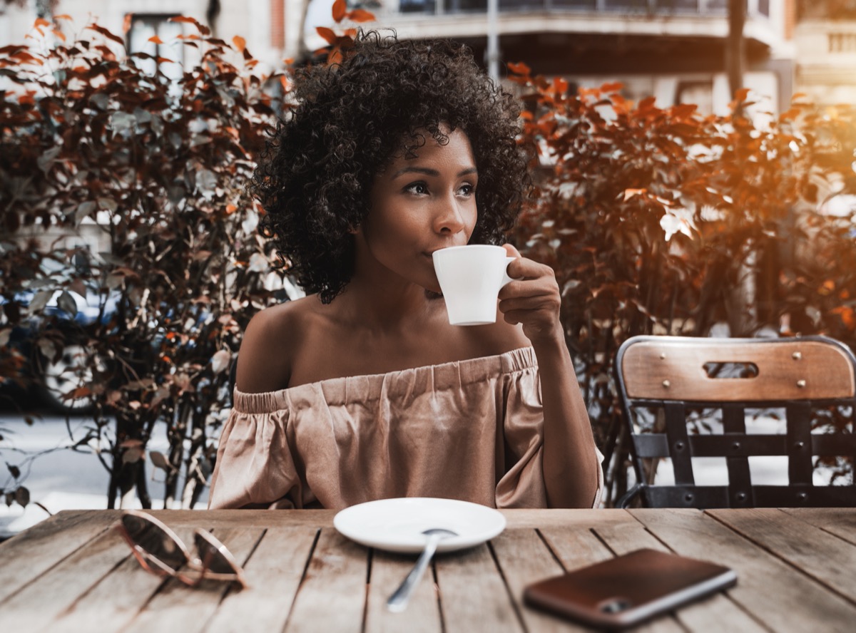 young woman in off-the-shoulder top drinking coffee outside