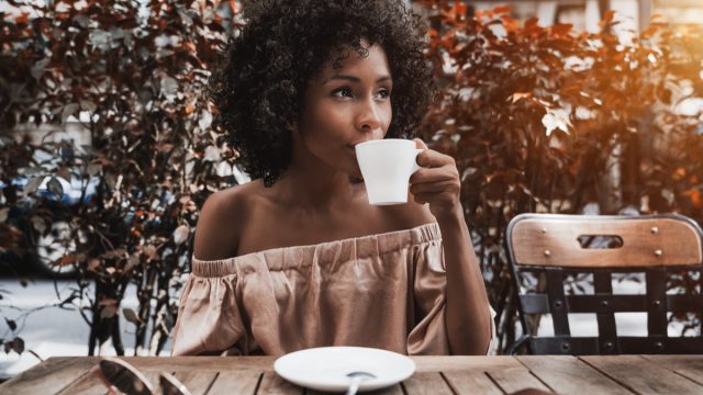 young woman in off-the-shoulder top drinking coffee outside