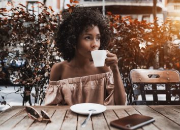 young woman in off-the-shoulder top drinking coffee outside