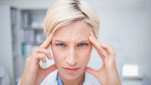 Portrait of female doctor suffering from headache in clinic