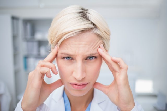 Portrait of female doctor suffering from headache in clinic