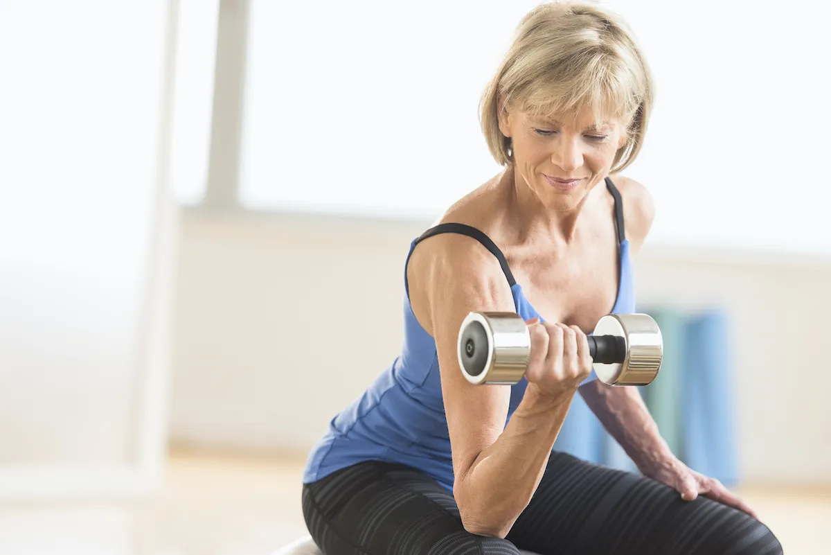 Fit mature woman lifting dumbbell while sitting at home