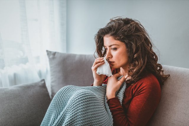 Sick woman with headache sitting under the blanket