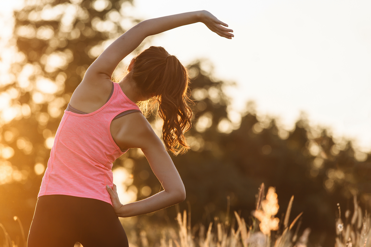 Young female workout before fitness training session at the park. Healthy young woman warming up outdoors. She is stretching her arms and looking away,hi key.