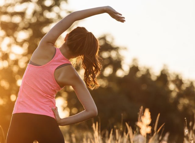 Young female workout before fitness training session at the park. Healthy young woman warming up outdoors. She is stretching her arms and looking away,hi key.