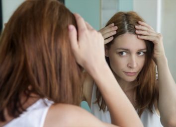 Woman examining her scalp and hair in front of the mirror.