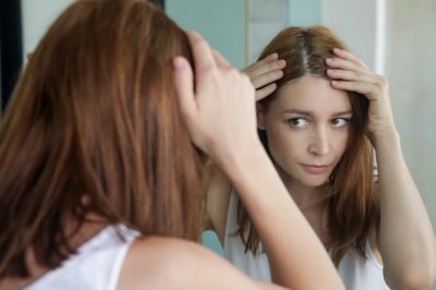 Woman examining her scalp and hair in front of the mirror.