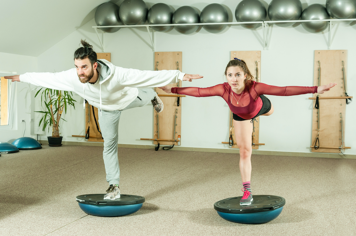 Young beautiful and attractive fitness couple workout on their balance by standing on the half ball on the one leg