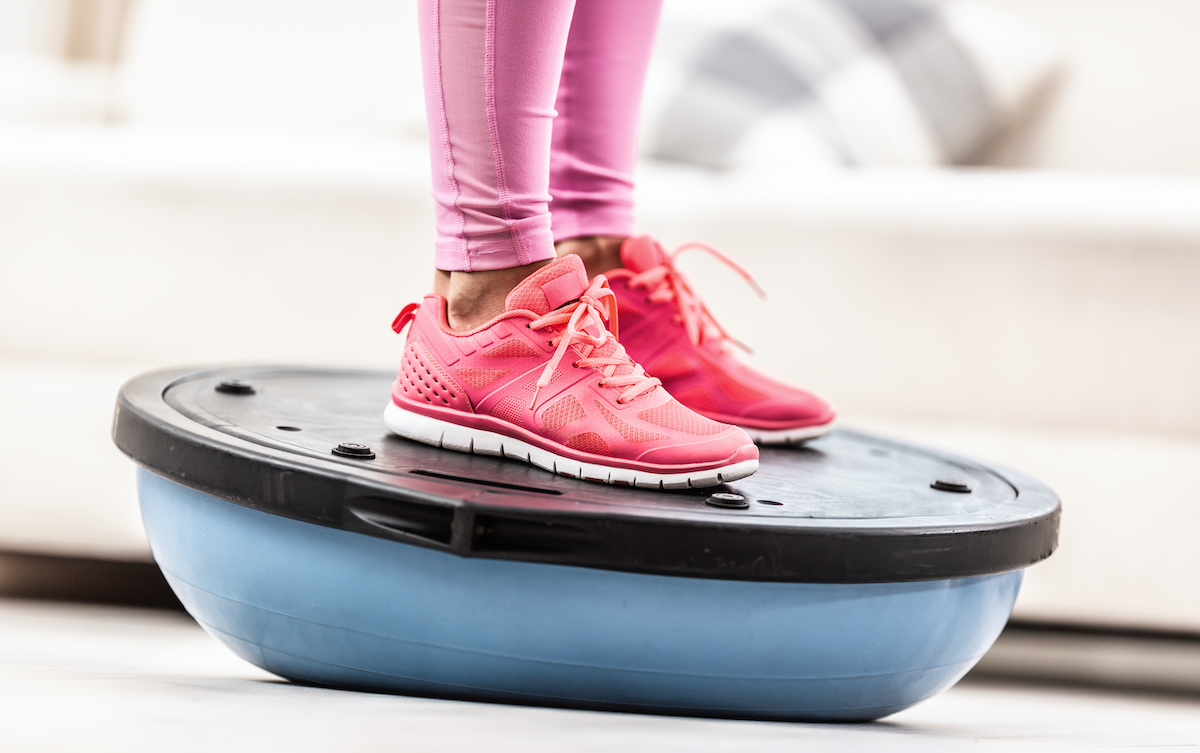 Woman in training shoes stands on a blue balance ball.