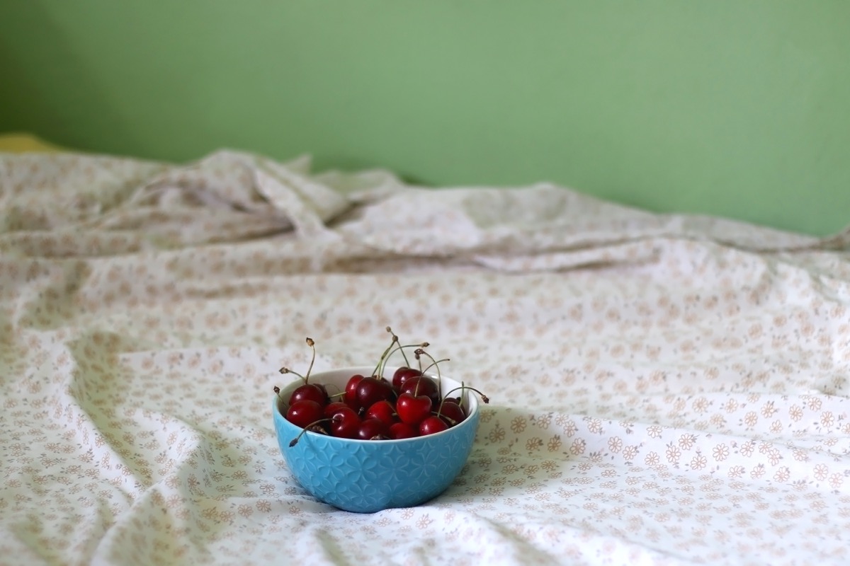 bowl of cherries on bed with floral sheets