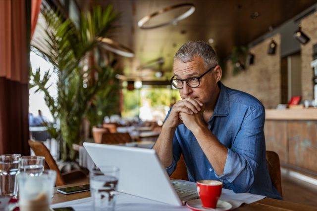 Mature man working on laptop while sitting at his working place in office.