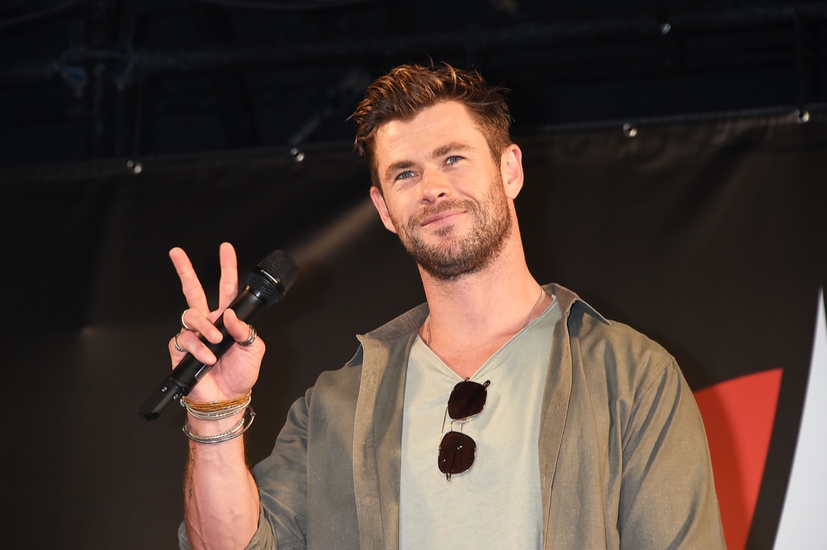 chris hemsworth in green jacket and gray t-shirt giving peace sign on stage