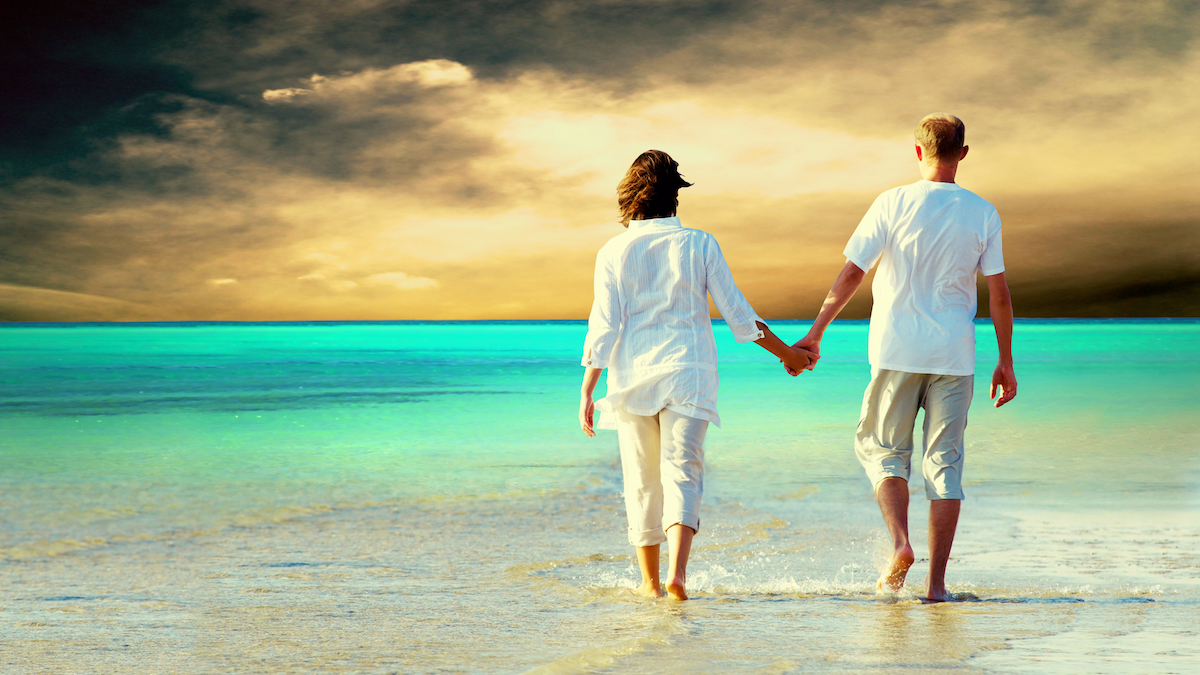 Rear view of a couple walking on the beach, holding hands.