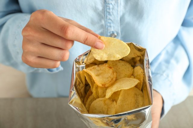 A person wearing a blue button down eats from a bag of chips