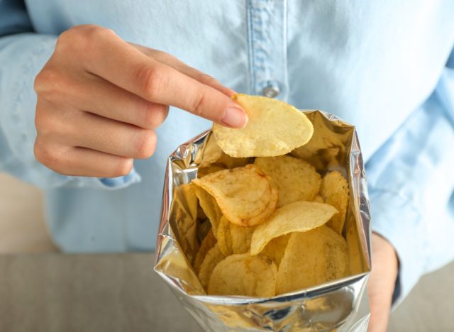 person in blue button down eating from bag of chips