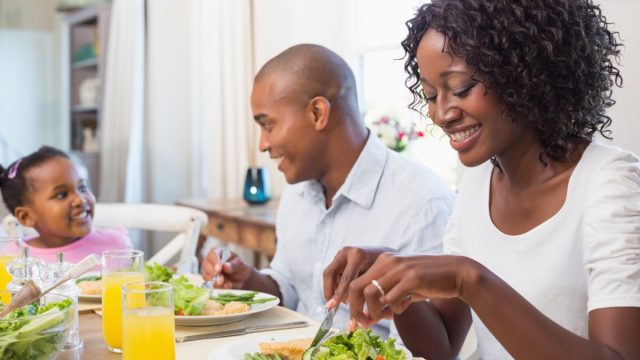 30-something woman and man and a young child eating salad at home