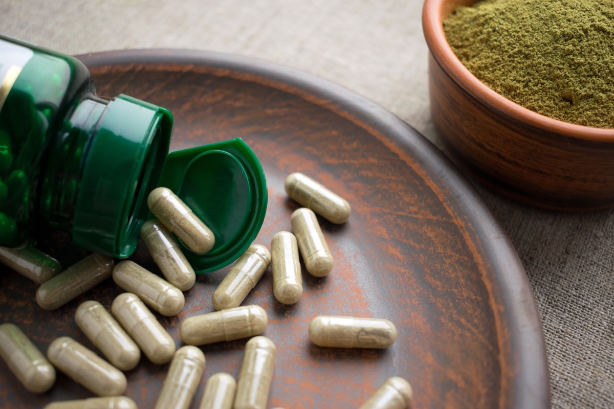 green tea supplement pills spilling out of green bottle onto wood plate