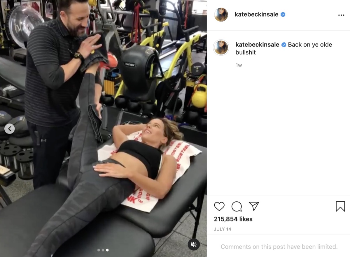kate beckinsale smiling at male trainer as he stretches her leg toward her head