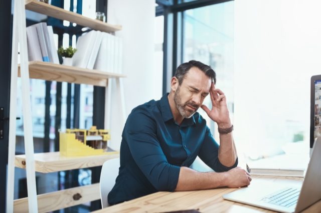 A mature businessman experiences a headache while working at a desk