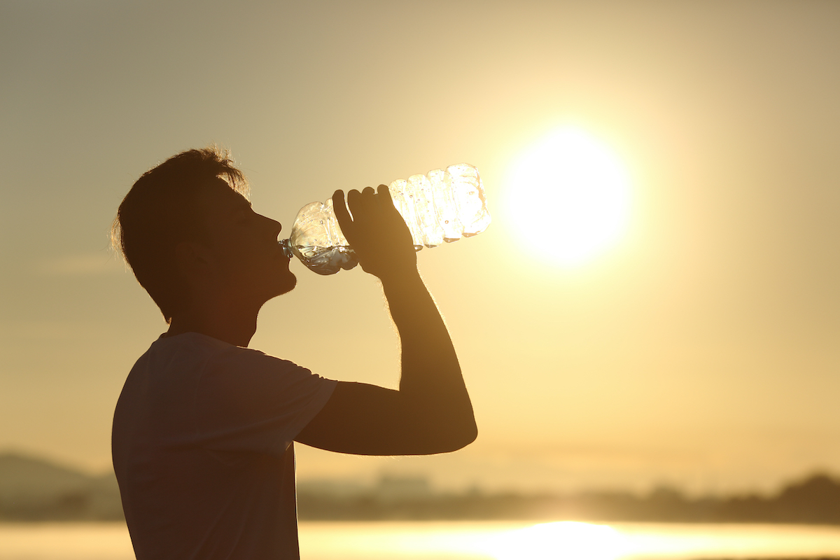 Profile of a fitness man silhouette drinking water from a bottle at sunset with the sun in the background