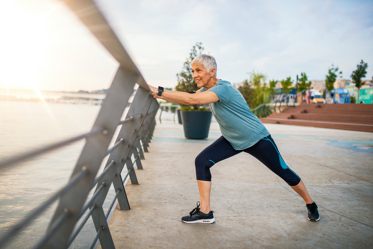 A senior woman stretches during her workout. Mature woman exercising. Portrait of fit elderly woman doing stretching exercise in park. Senior sportswoman making stretch exercises