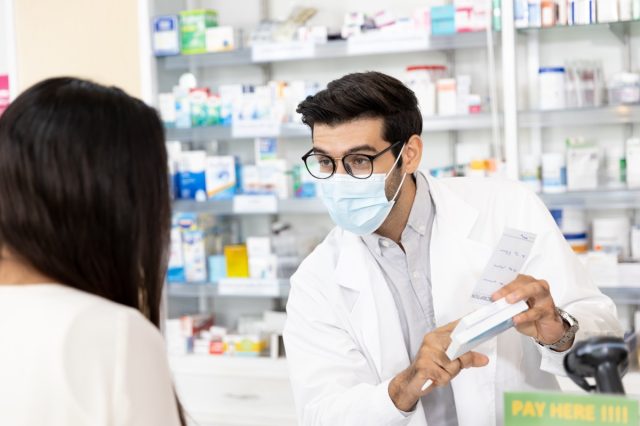 Farmacéutico que usa una máscara higiénica protectora y hace recomendaciones de medicamentos en la farmacia moderna