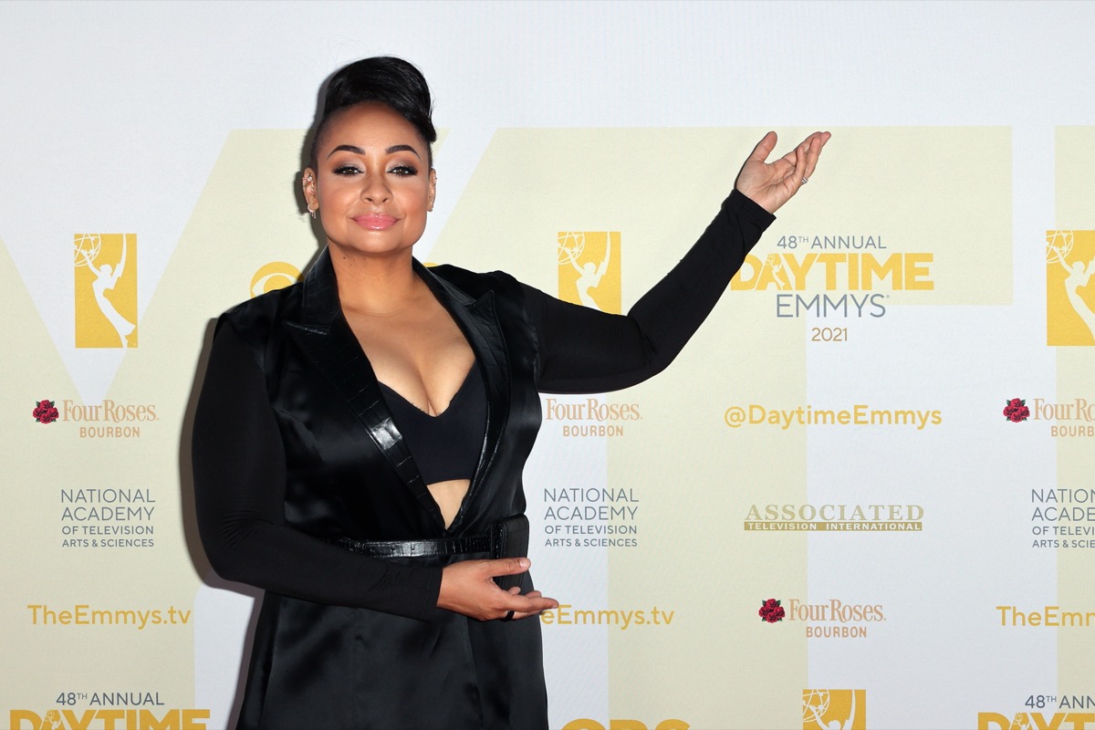 raven symone in black jacket and bandeau on red carpet with arm in the air