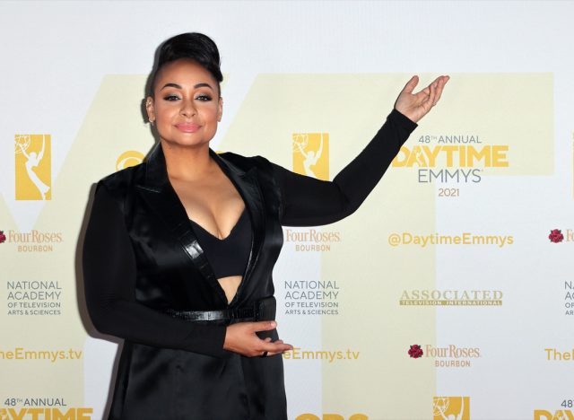 raven symone in black jacket and bandeau on red carpet with arm in the air