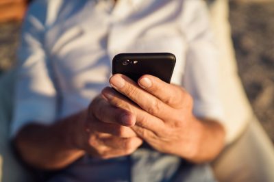 Senior man using smartphone during sunset. Close up