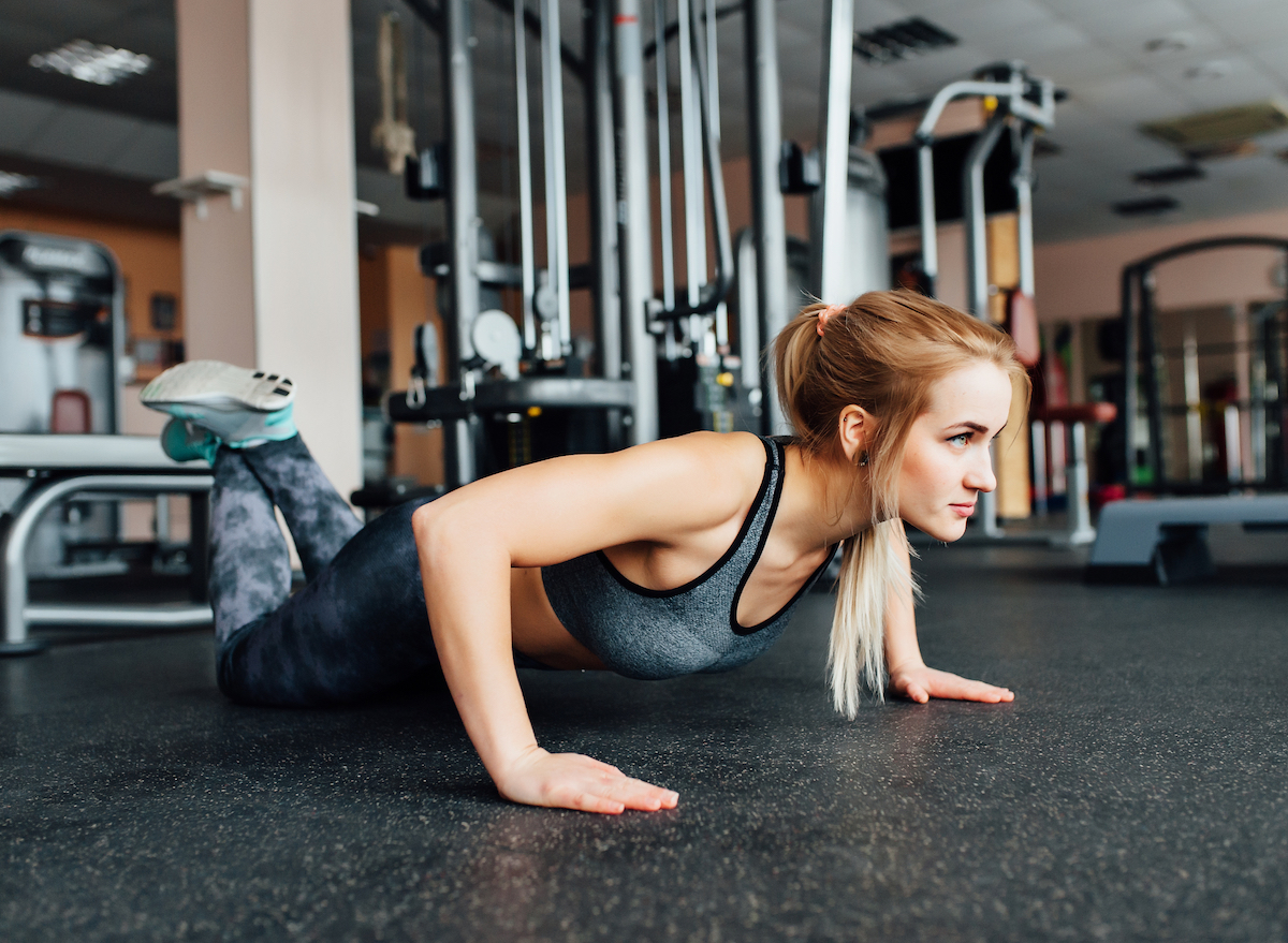 woman with long hair in gym doing a pushup from her knees 