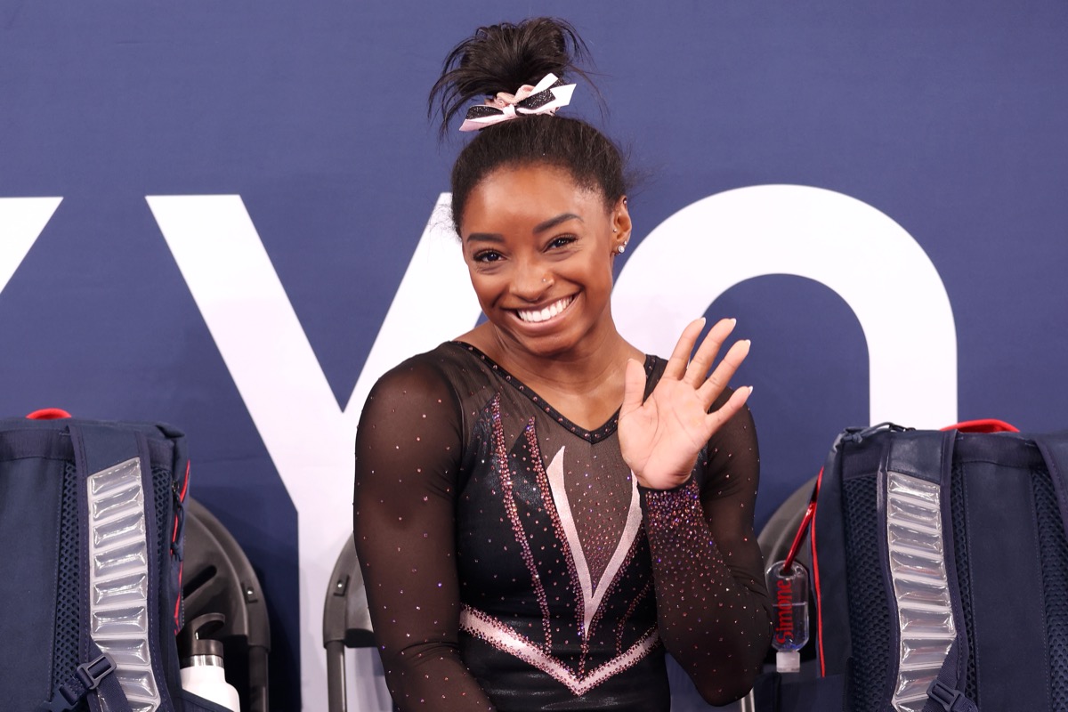 simone biles smiling and waving while wearing black leotard