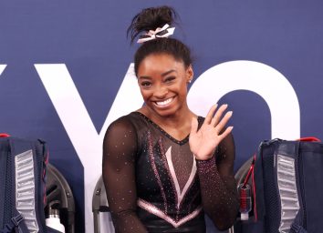 simone biles smiling and waving while wearing black leotard