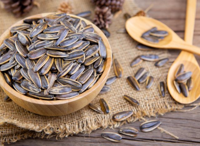 wooden bowl of sunflower seeds on piece of burlap next to two wooden spoons