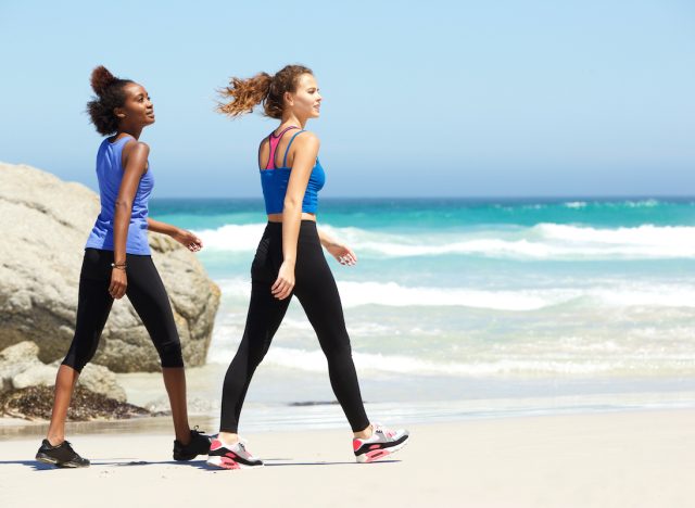 Side portrait of two young sporty women walking on the beach