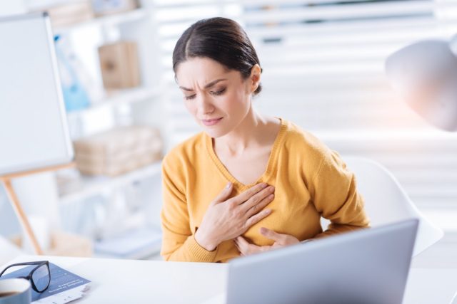 Woman touching her heart while sitting at the table in her big office.