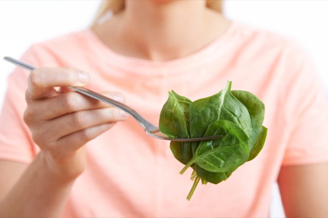 woman eating raw spinach on fork