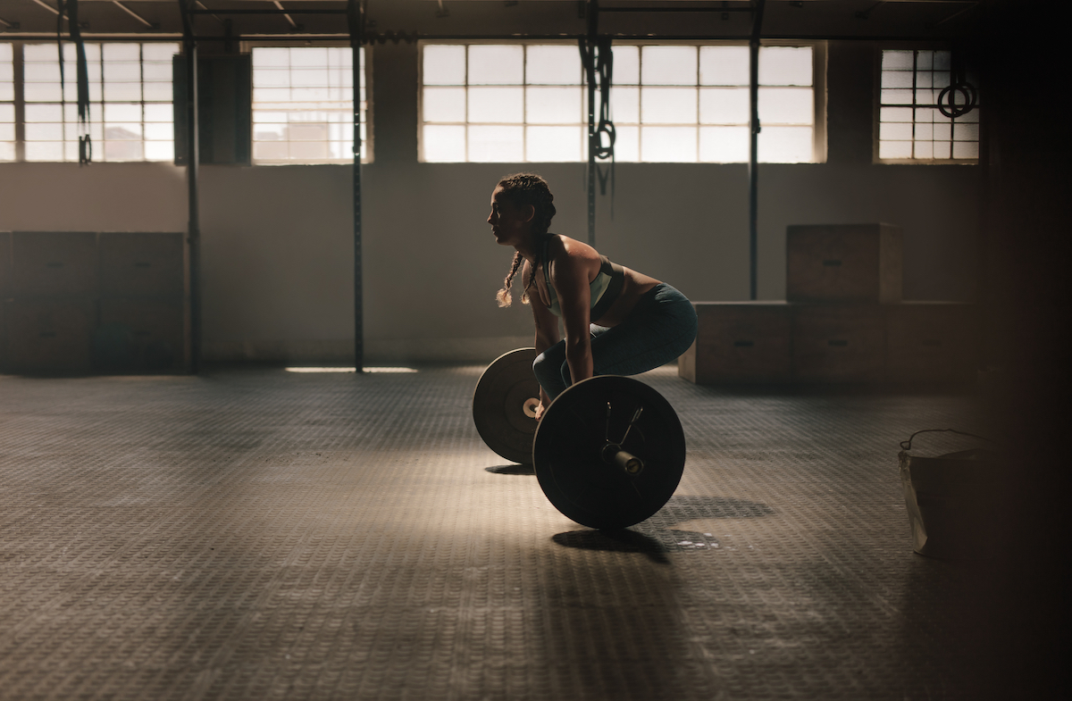 Muscular female athlete lifting heavy weights at gym. Fitness woman doing weightlifting exercise at health club.