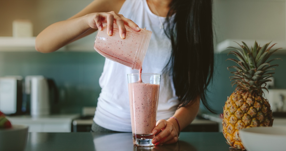 young woman pouring smoothie from blender into cup