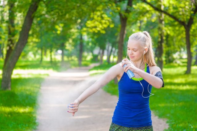 A woman spraying insect repellents on skin before running