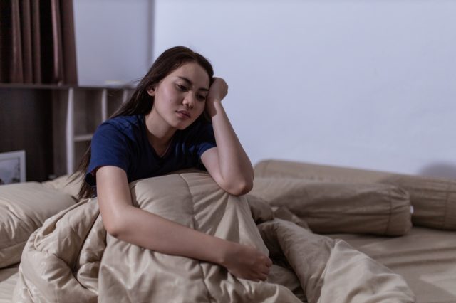 a young woman sits in bed and cannot sleep