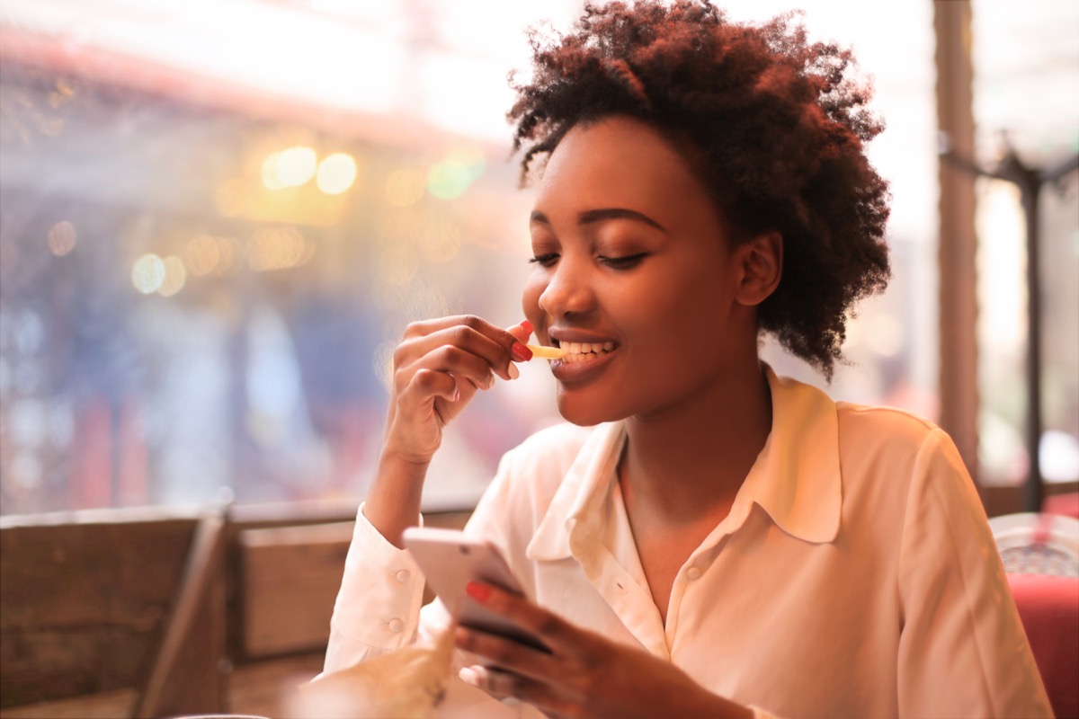 young woman looking at phone and eating fries