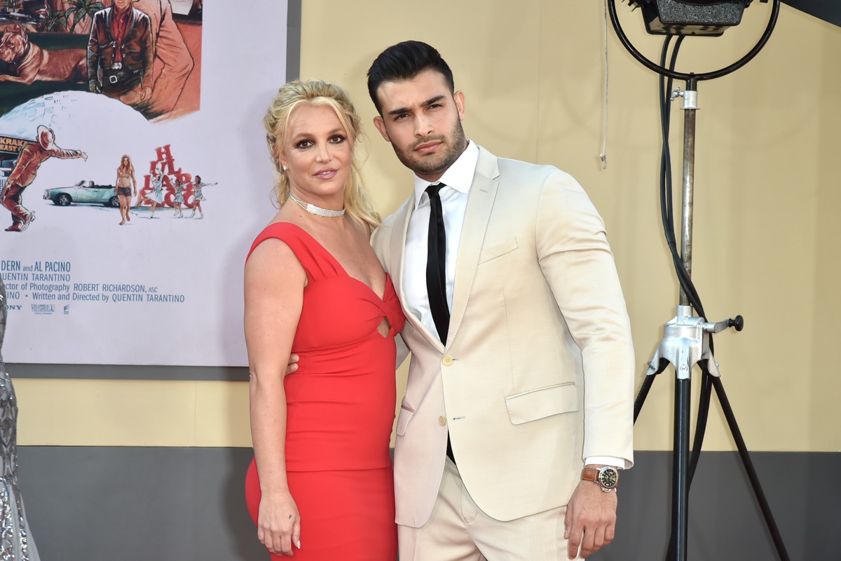 sam asghari in a tan suit standing next to britney spears in red dress on red carpet